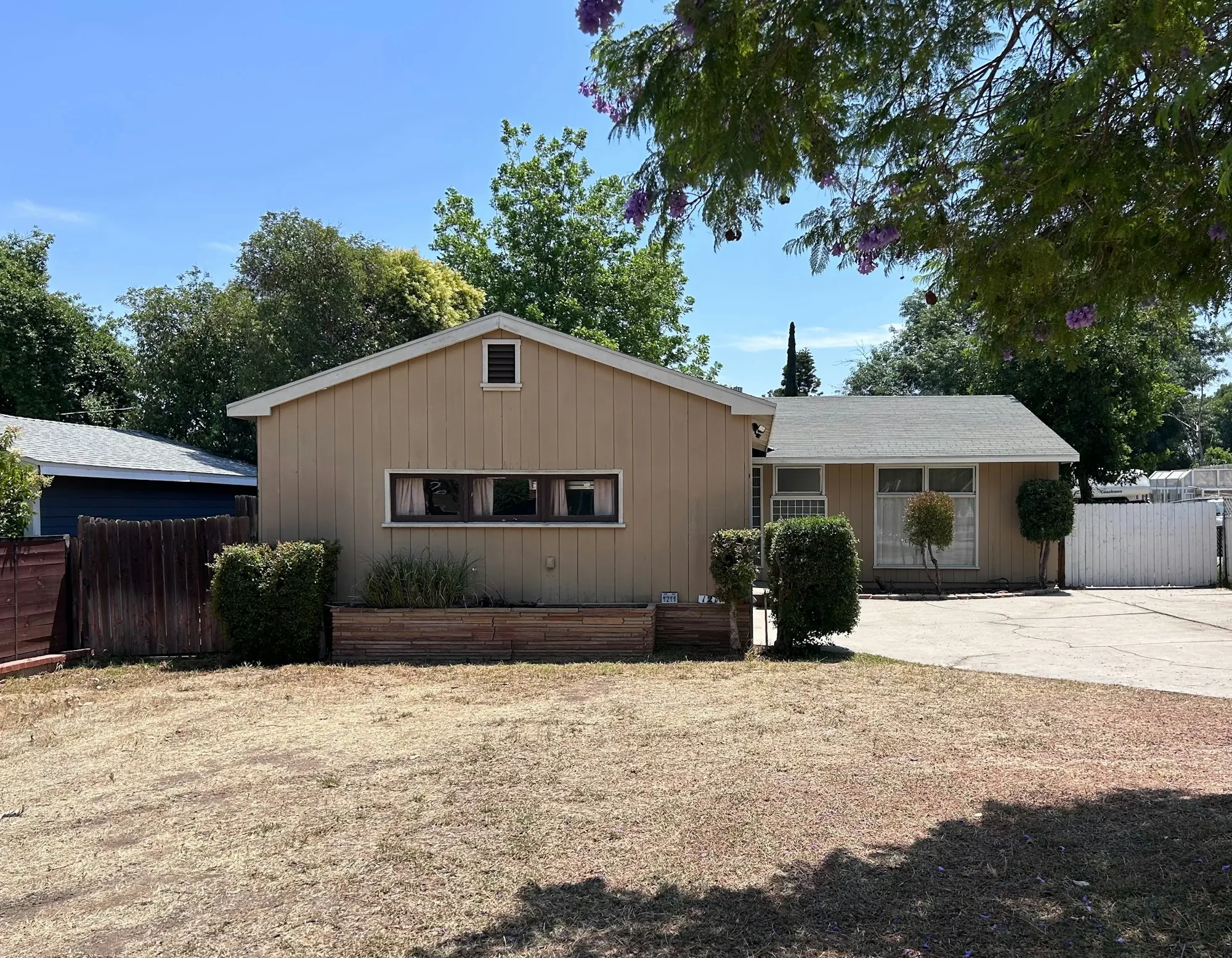 Single-story ranch home with a gravel driveway and shade trees
