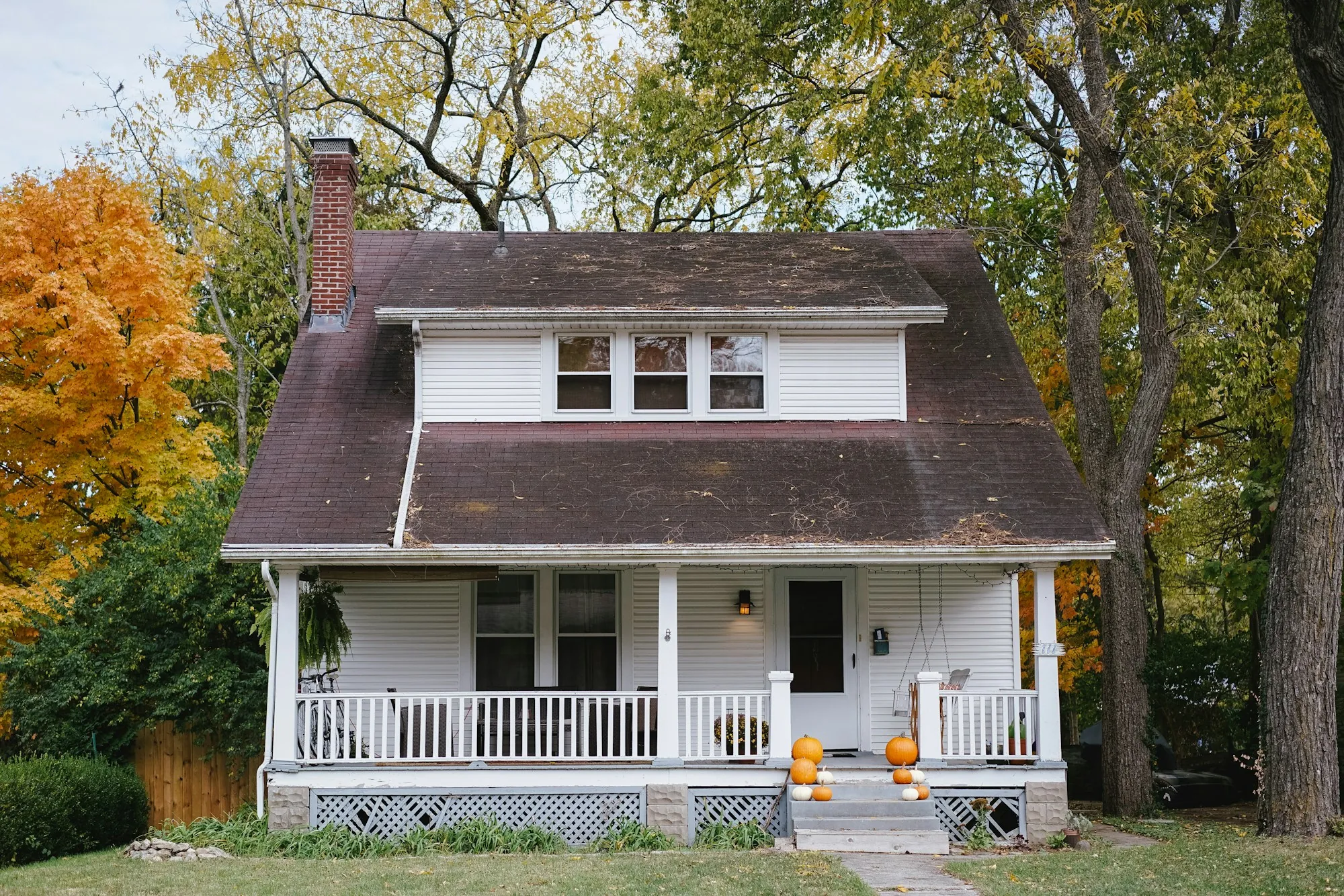 Craftsman bungalow with a brown shingle roof and white porch in autumn